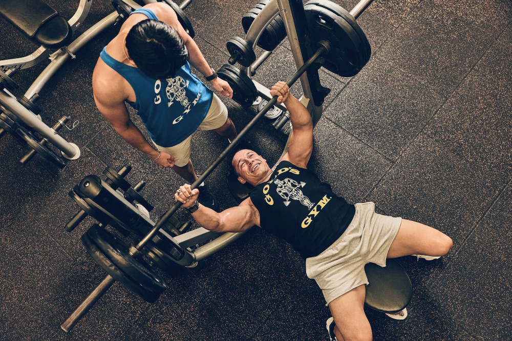 Aluno auxiliado por spotter no supino na Gold's Gym